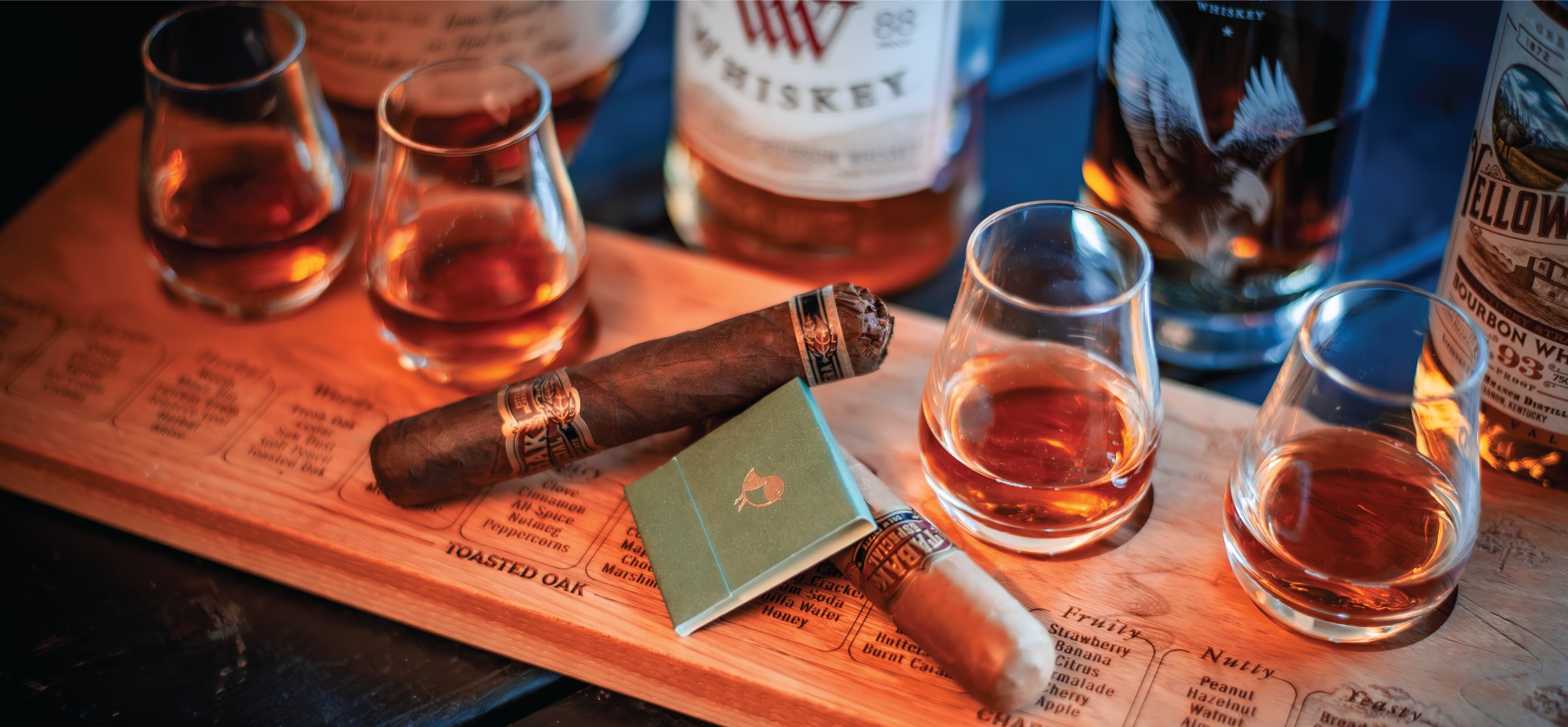 Four whiskey tasting glasses filled with bourbon sitting on a taster board with a cigar resting in the middle
